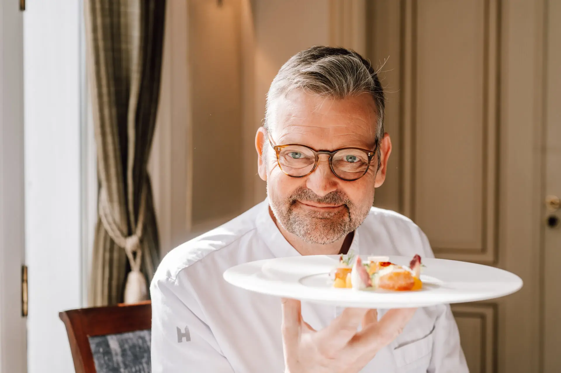 Koch Thomas Martin hält einen Teller mit Essen in die Kamera und lächelt.