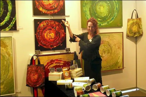 Angela Scherer-Kern Eine Frau steht vor einer Wand mit vielen mit Gemälden.