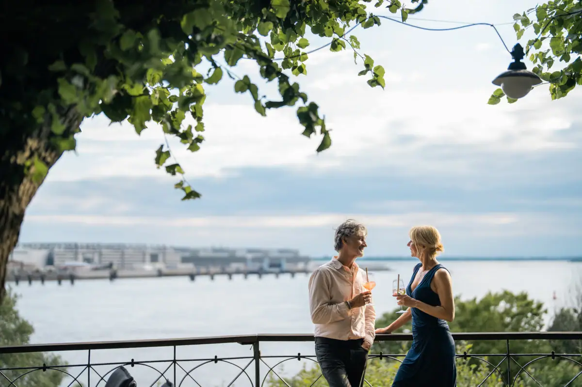 Ausblick Lindenterrasse Ein Mann und eine Frau stehen an dem Geländer von der Lindenterrasse und schauen auf die Elbe.