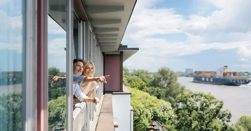 Un homme et une femme regardent l'Elbe depuis une fenêtre de la suite de l'hôtel Louis C. Jacob sur l'Elbe.