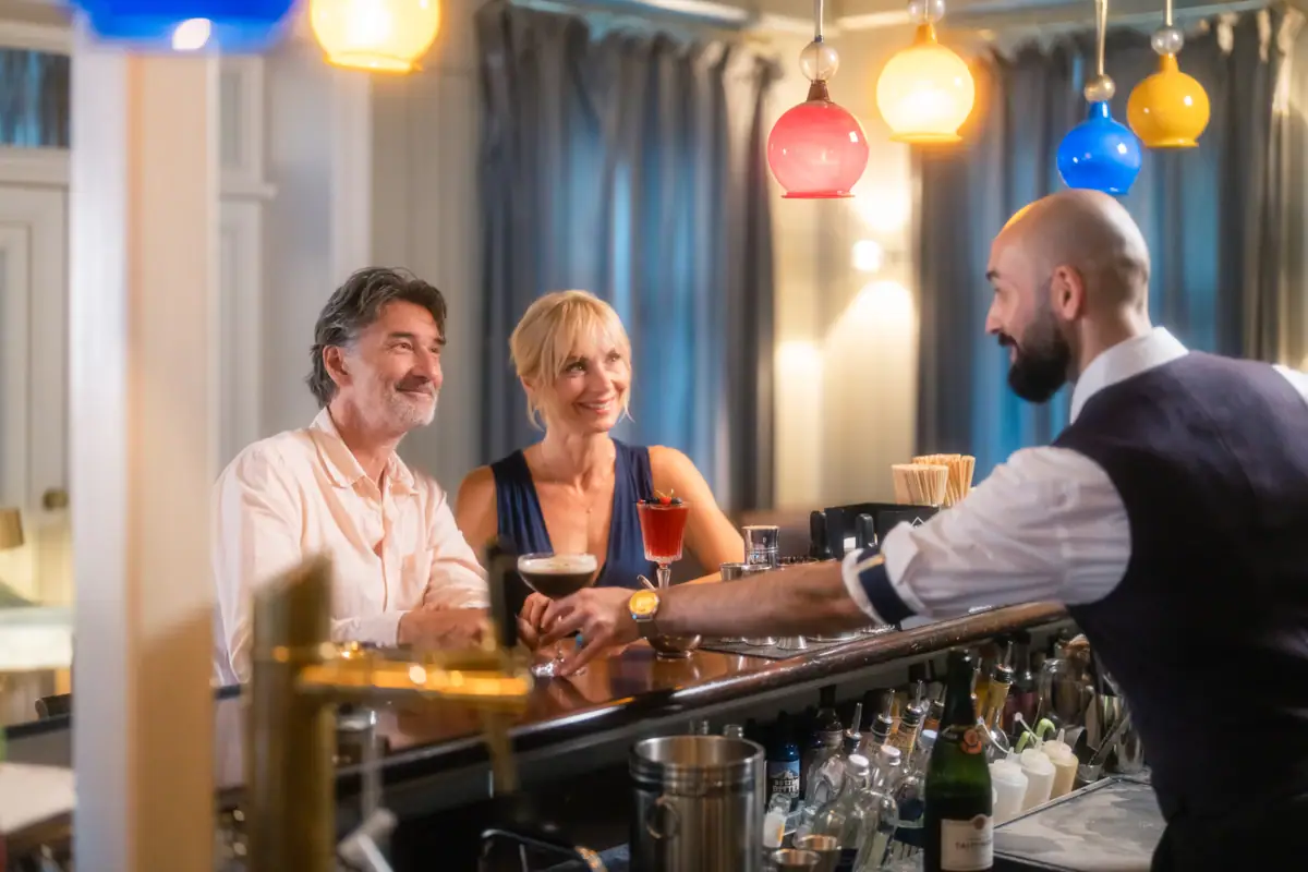 Ein Paar sitzt lächelnd am Tresen der Jacobs Bar und wird von einem Barkeeper bedient. 