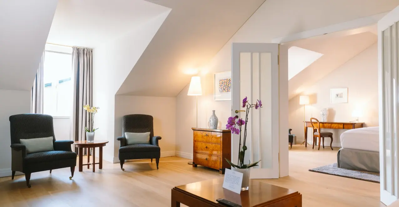 Chambre d'hôtel au Louis C. Jacob avec un sol en bois, une table, des chaises et un vase avec des fleurs.