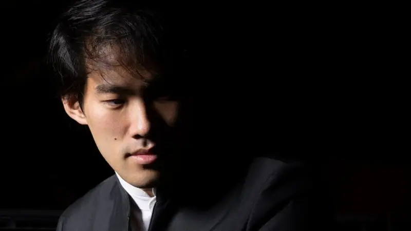 Pianist Bruce Liu sitzt halb im Schatten und schaut nach unten.