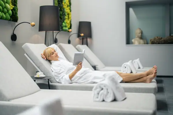 Eine Frau liegt auf einer Chaiselongue und liest ein Buch in einem Wellnessbereich.