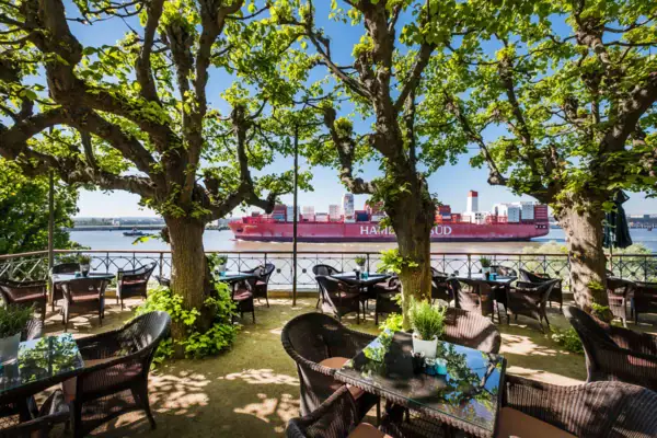 Des tables et chaises disposées sous des arbres près d'un plan d'eau.