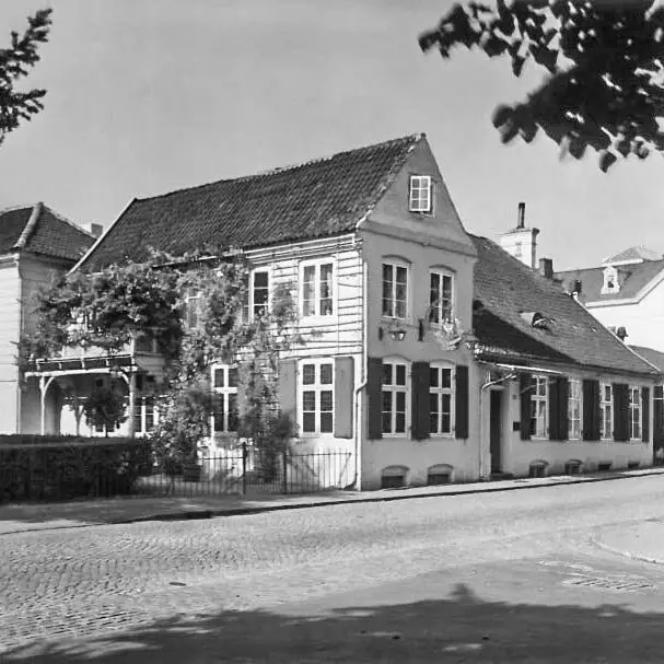 Ein altes Schwarz-Weiß-Foto vom Louis C. Jacob Hotel mit einem Zaun und einer Hecke davor.