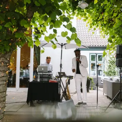 Un homme en costume blanc chantant dans un micro sous un arbre.