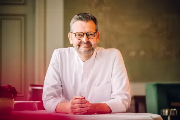 Thomas Martin Mann sitzt am Tisch und lächelt offen