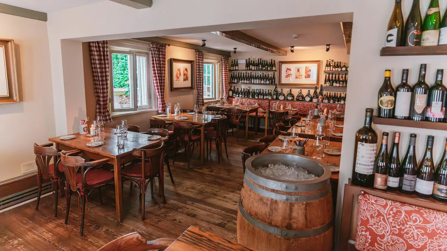 Vue intérieure d'une salle à manger avec des tables, des chaises et des bouteilles de vin.