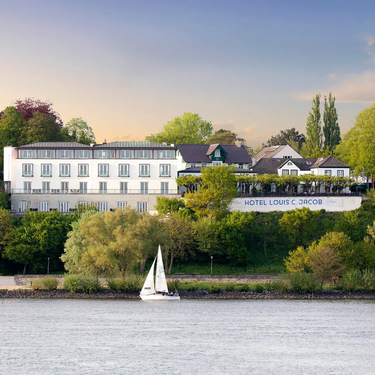 Louis C. Jacob  Das Louis C. Jacob Hotel an der Elbe mit einem Segelboot davor im Wasser.