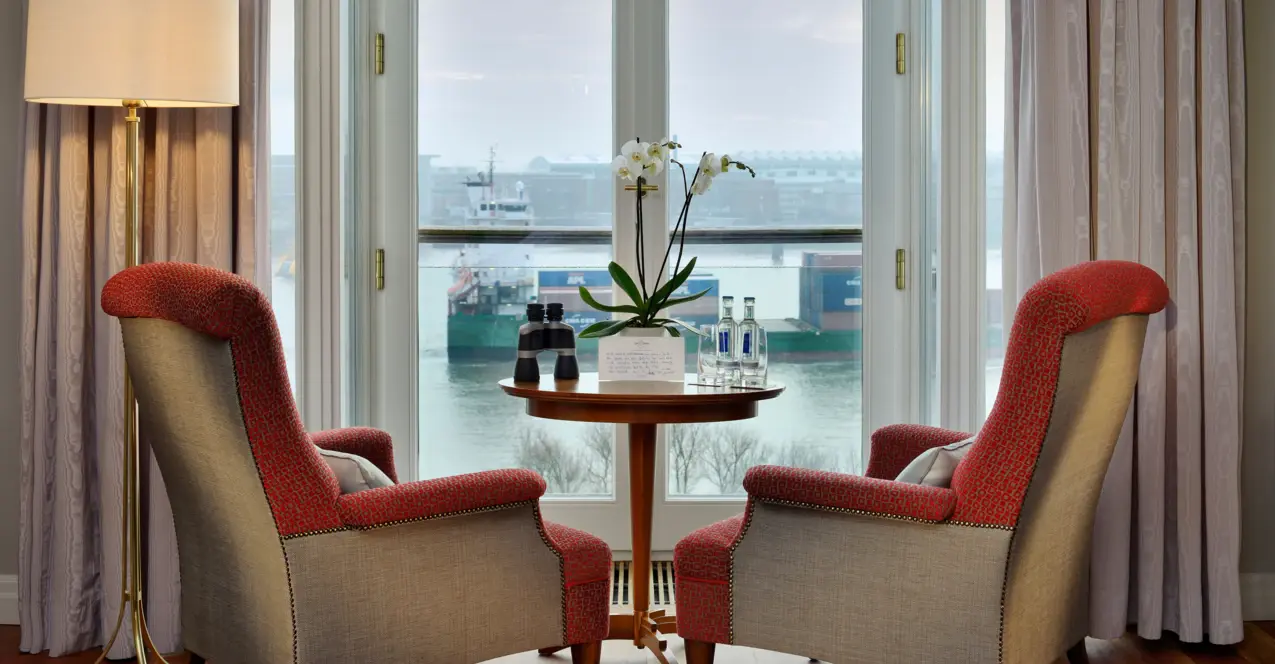 Chambre d'hôtel au Louis C. Jacob avec deux chaises et une table devant une fenêtre avec vue sur l'Elbe.