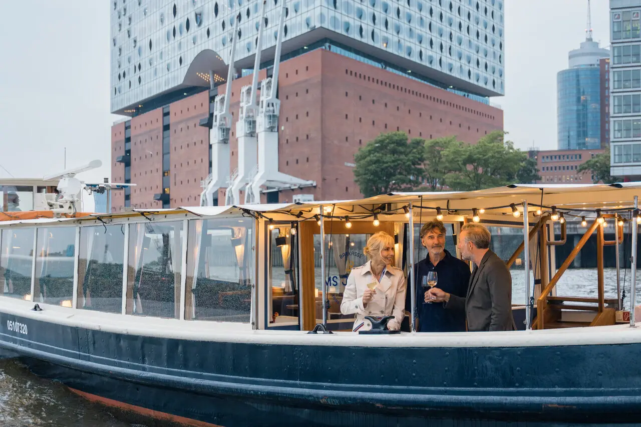 Eine Gruppe von Menschen auf einer Barkasse vor der Elbphillharmonie Hamburg.