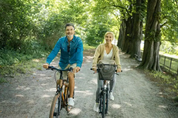 Un homme et une femme font du vélo sur un chemin bordé d'arbres.