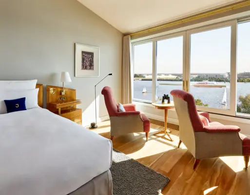 Chambre avec un lit et des chaises, fenêtre donnant sur l'eau.