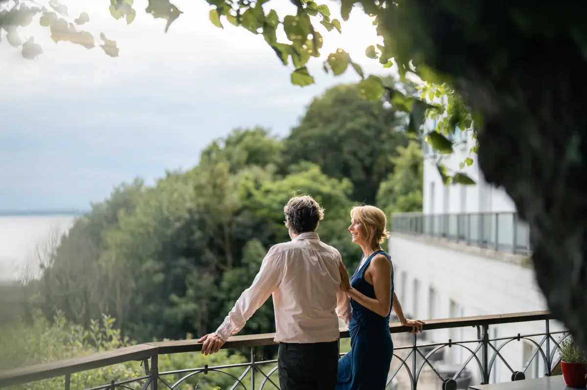 Ein Mann und eine Frau stehen an der Reling der Lindenterrasse des Hotels Louis C. Jacob und schauen auf die Elbe.