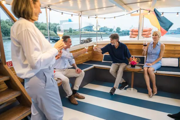 Mehrere Personen sitzen und stehen im überdachten Außenbereich der Barkasse MS Jacob.