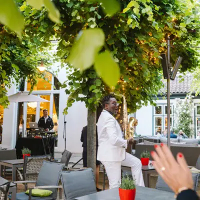 Un homme en costume blanc joue du saxophone sous un arbre.