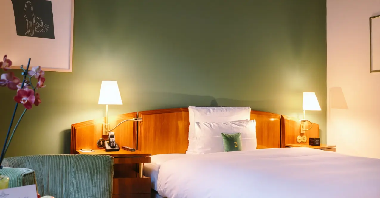 Un lit avec une tête de lit en bois et des lampes dans une chambre individuelle aménagée avec style. à l'hôtel Louis C. Jacob à Hambourg.